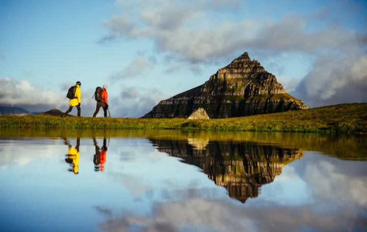 Hikers by a small lake, with a mountain reflected in the water